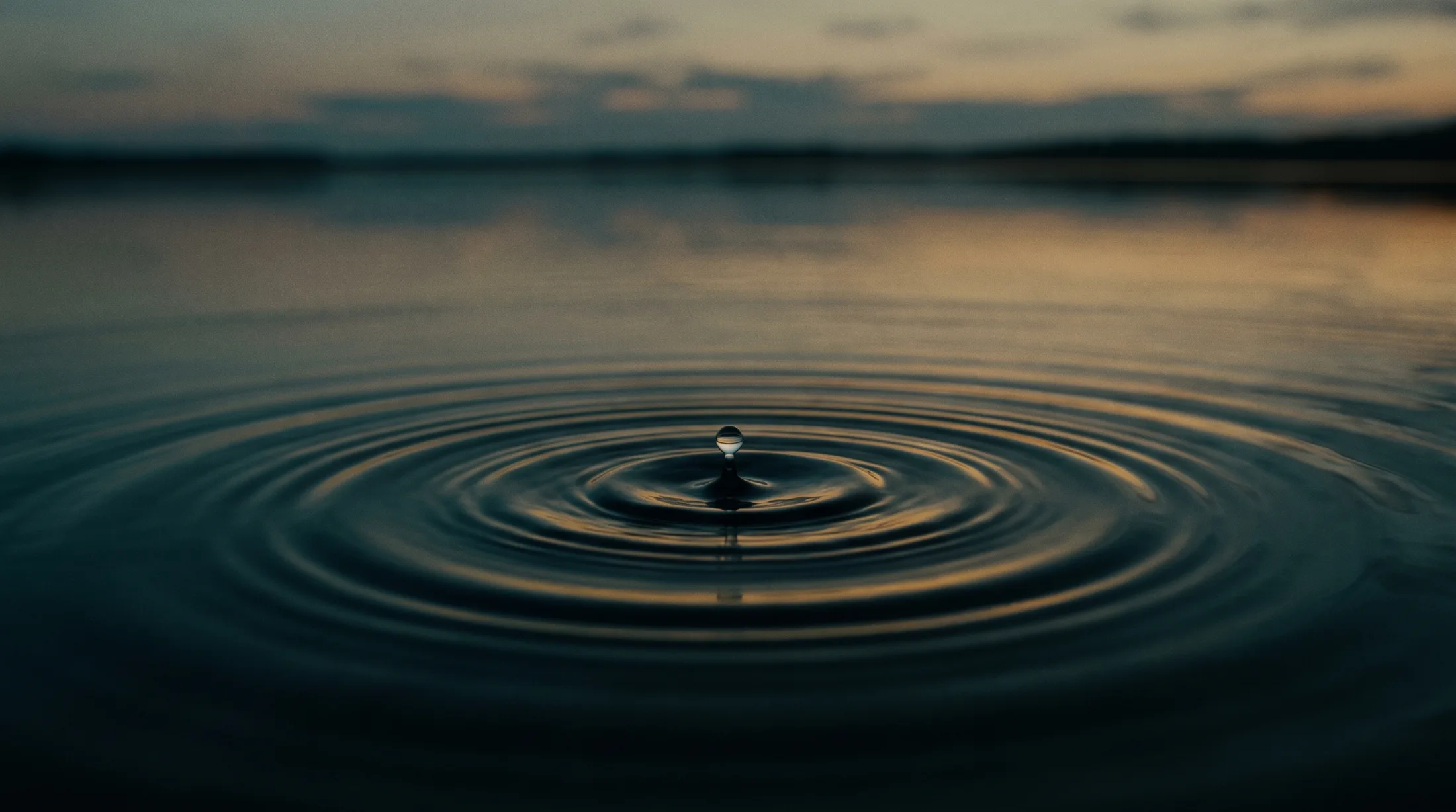 Gota caindo em água escura e formando ondas ao entardecer